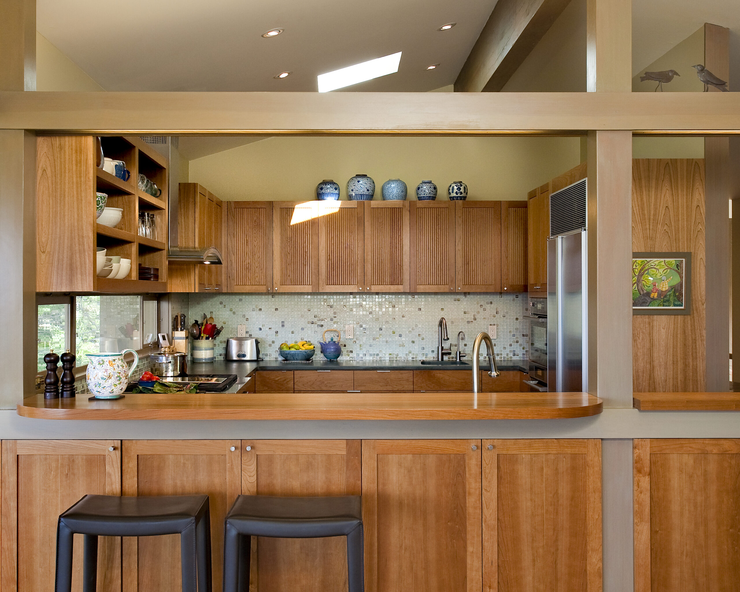 Broadview kitchen remodel with cherry cabinetry, a curved wood bar counter with two stools, a glass mosaic tile backsplash, and a skylight