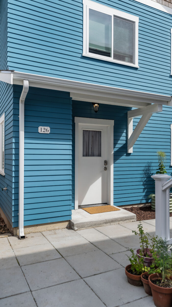Leschi DADU entry with blue lap siding, a white door under a bracketed awning, and a paver patio