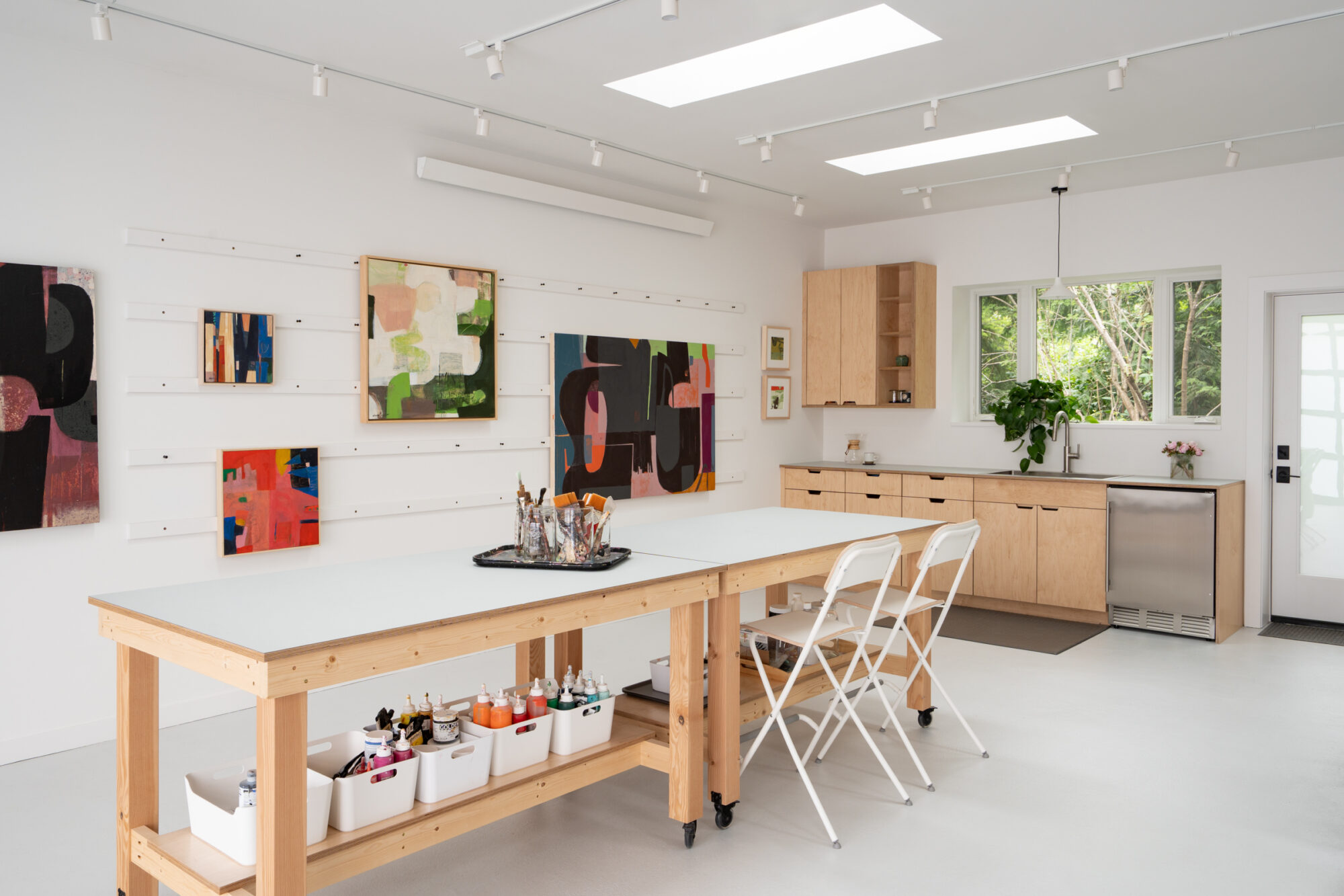 Innis Arden art studio with long wood work tables, paintings on the walls, and a sink along the back wall