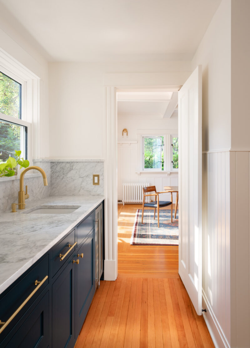 Capitol Hill kitchen galley with navy cabinets, marble counters, and a brass faucet leading to the dining room