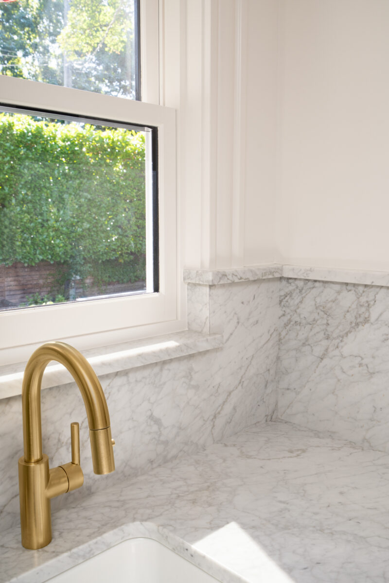 Brass faucet at a marble sink below a window in a Capitol Hill kitchen