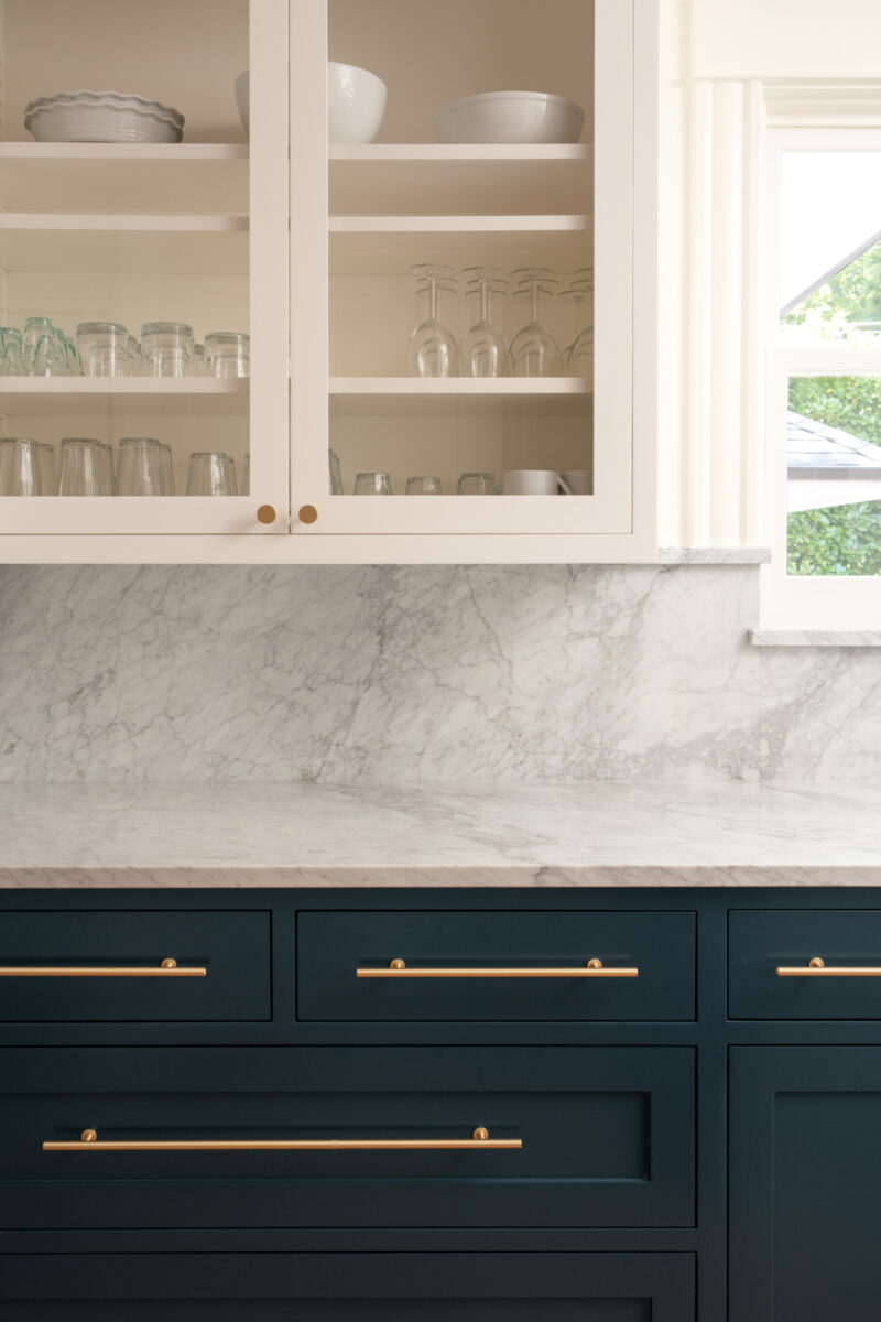 Glass-front cabinets with glassware above navy drawers and marble counters in a Capitol Hill kitchen