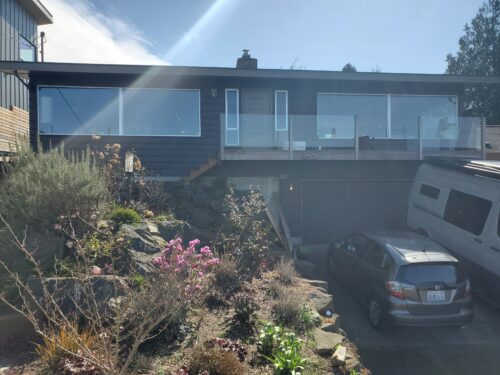 Before photo of a North Beach mid-century home with a dark exterior, glass railing, and steep driveway